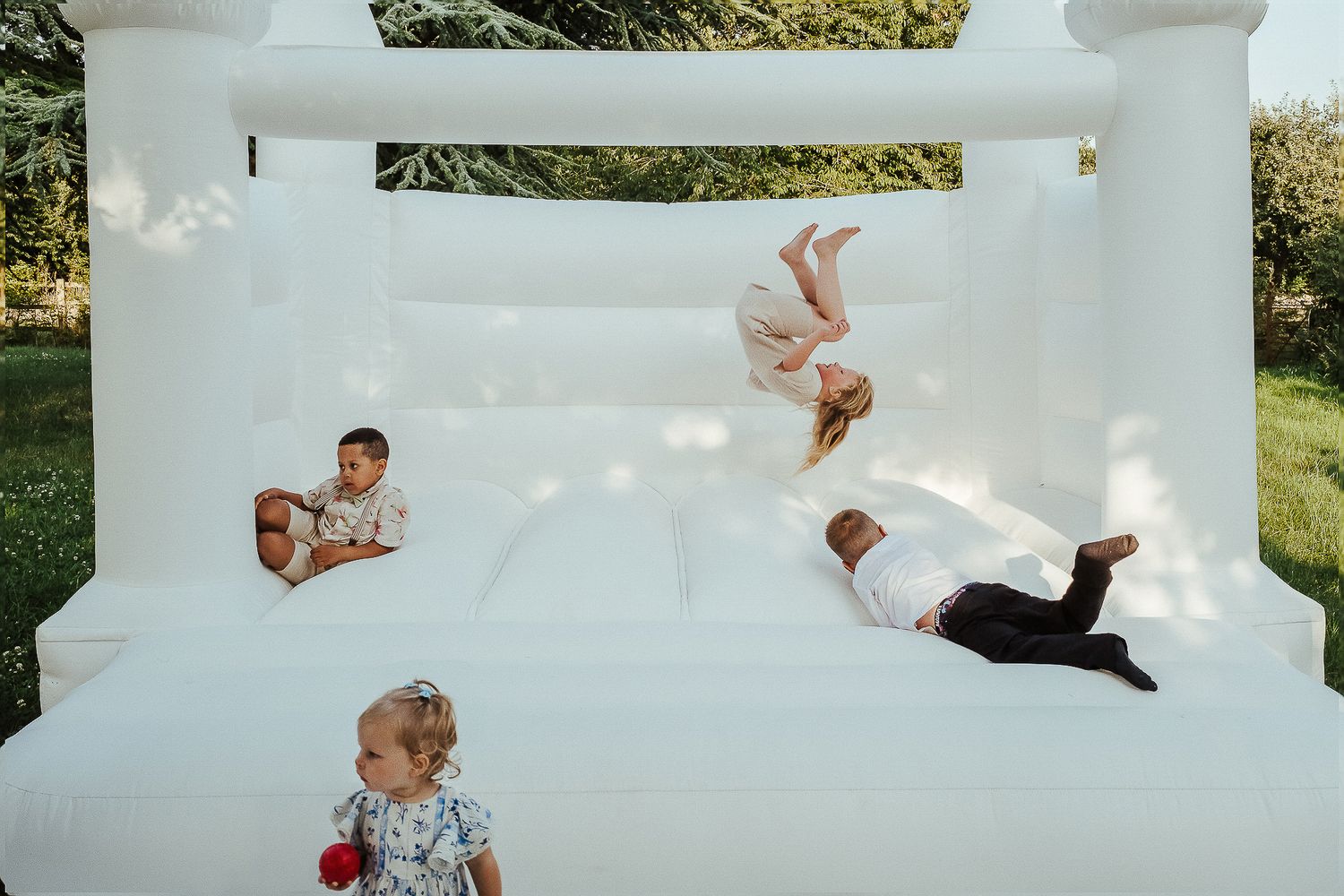 Children and adults playing and jumping inside a white bouncy castle at an outdoor event.