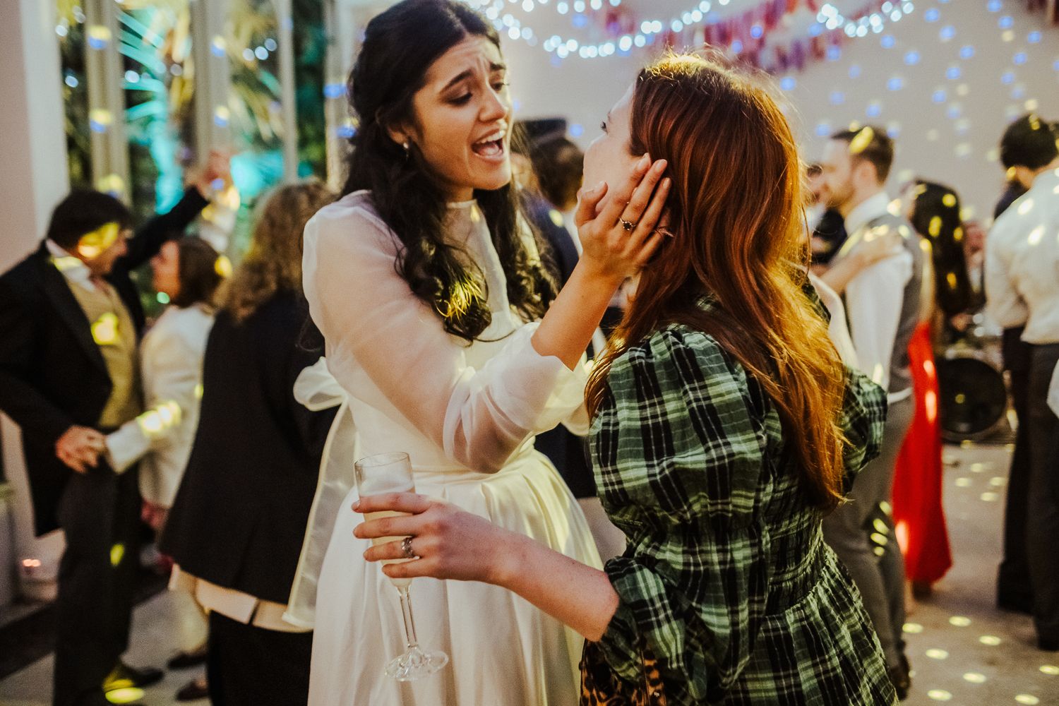 Two attendees sharing an emotional moment during a celebration with twinkling lights in the background.