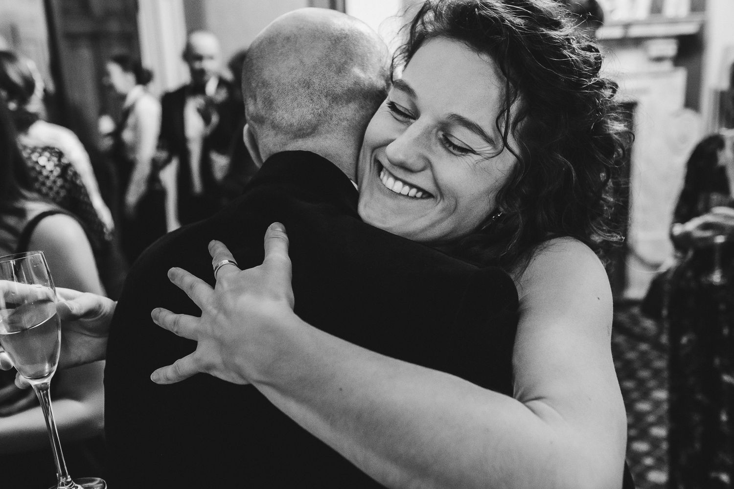 A joyful black and white candid moment of two people embracing at a celebration.