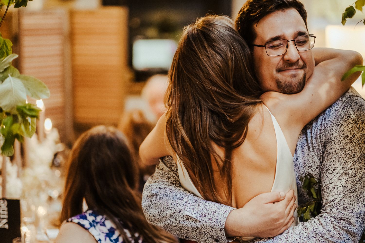 Emotional embrace shared during a wedding reception with warm lighting and floral decor.
