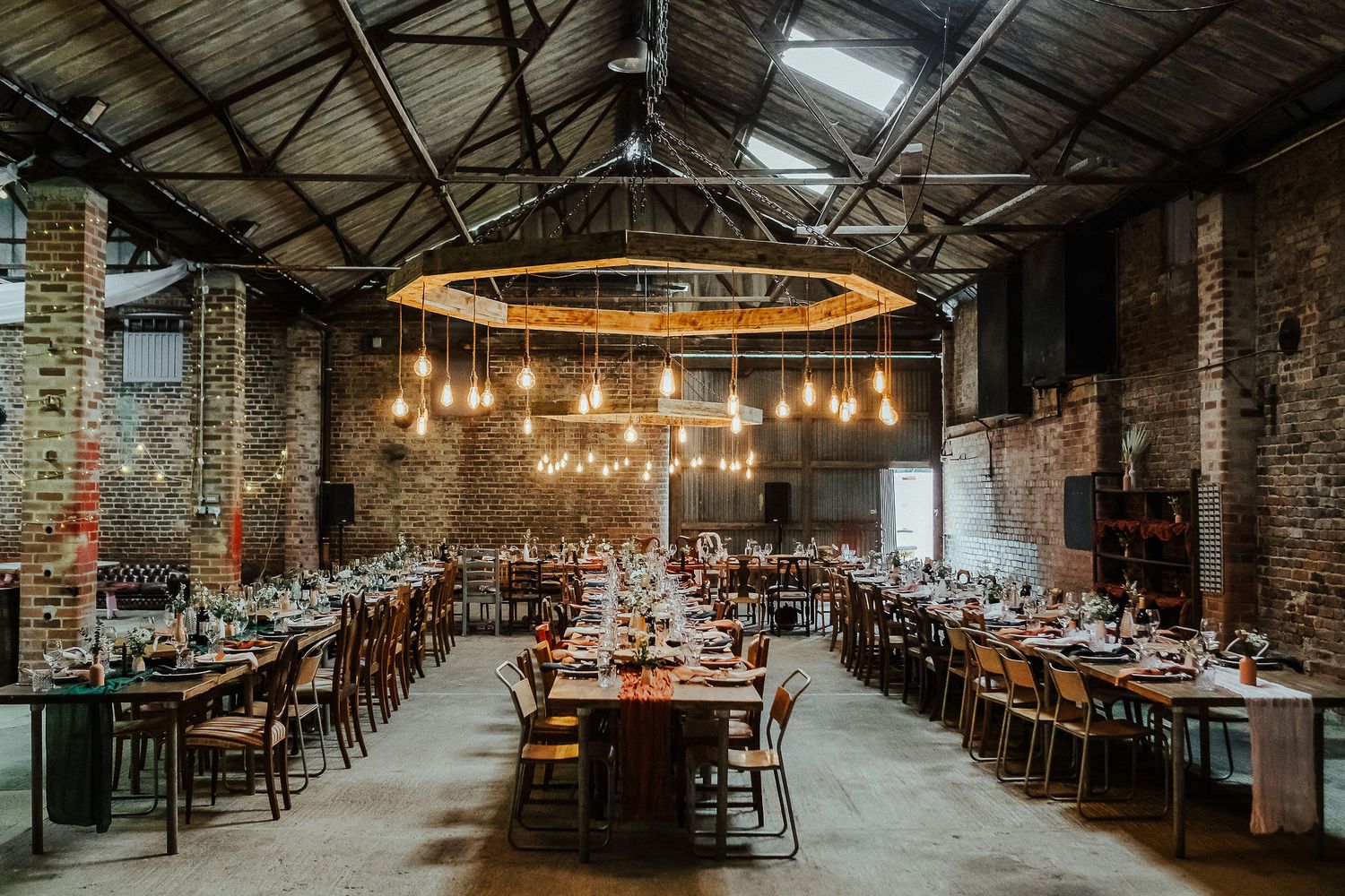 Industrial venue interior with exposed brick walls and warm hanging lights set for wedding reception.