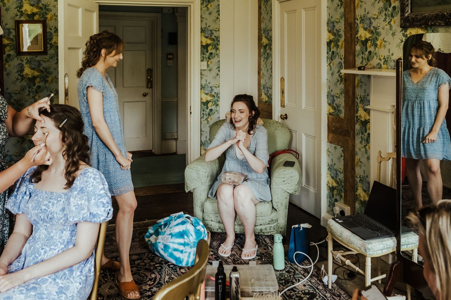 Wedding preparation scene in vintage wallpapered room with bridesmaids getting ready.