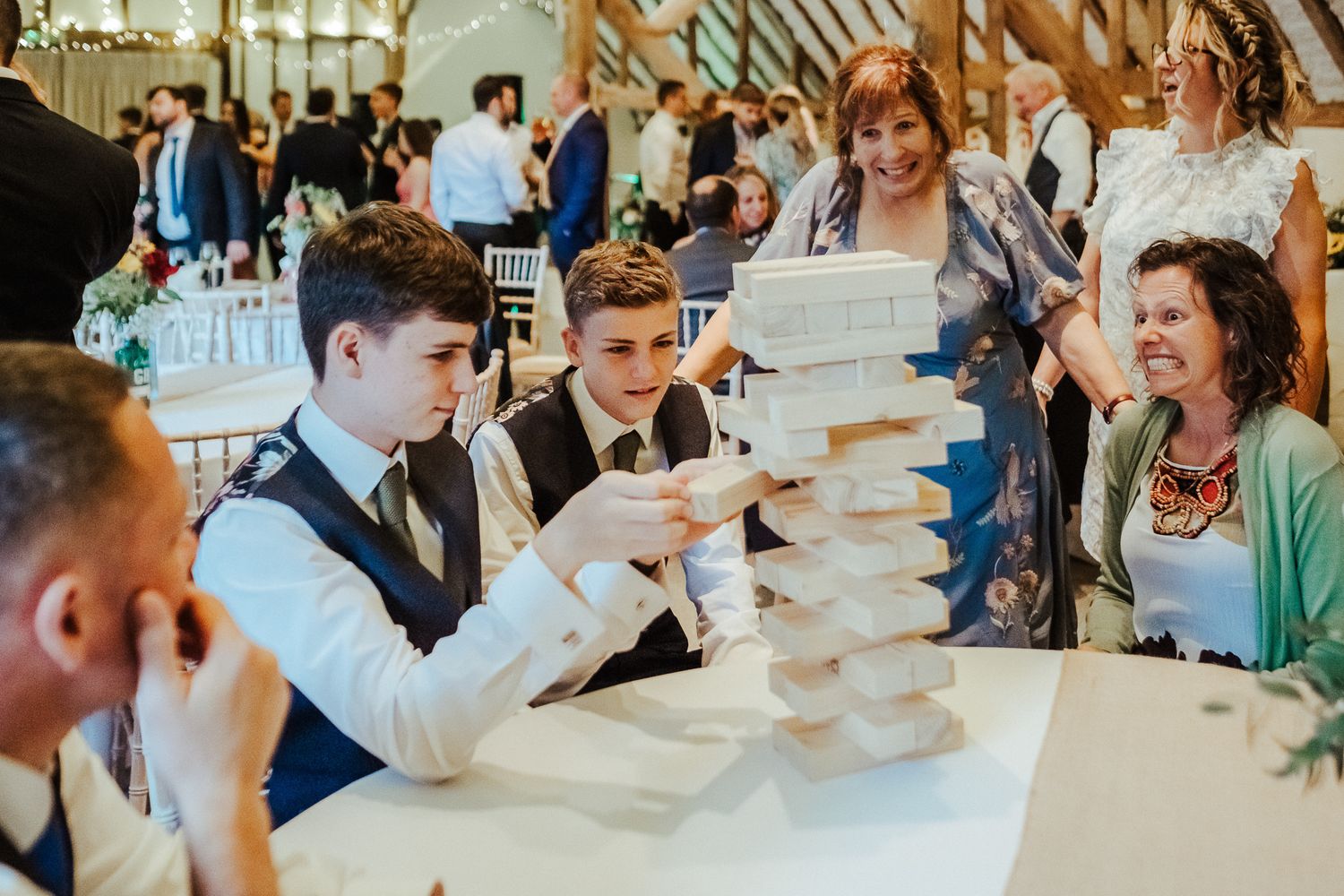 Wedding guests playing an intense game of Jenga at a reception table.