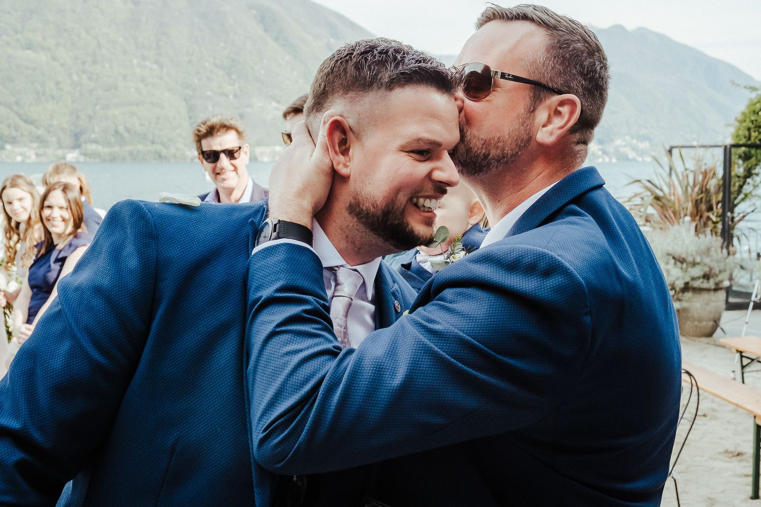 An emotional moment shared between two people in navy suits against a mountain backdrop.