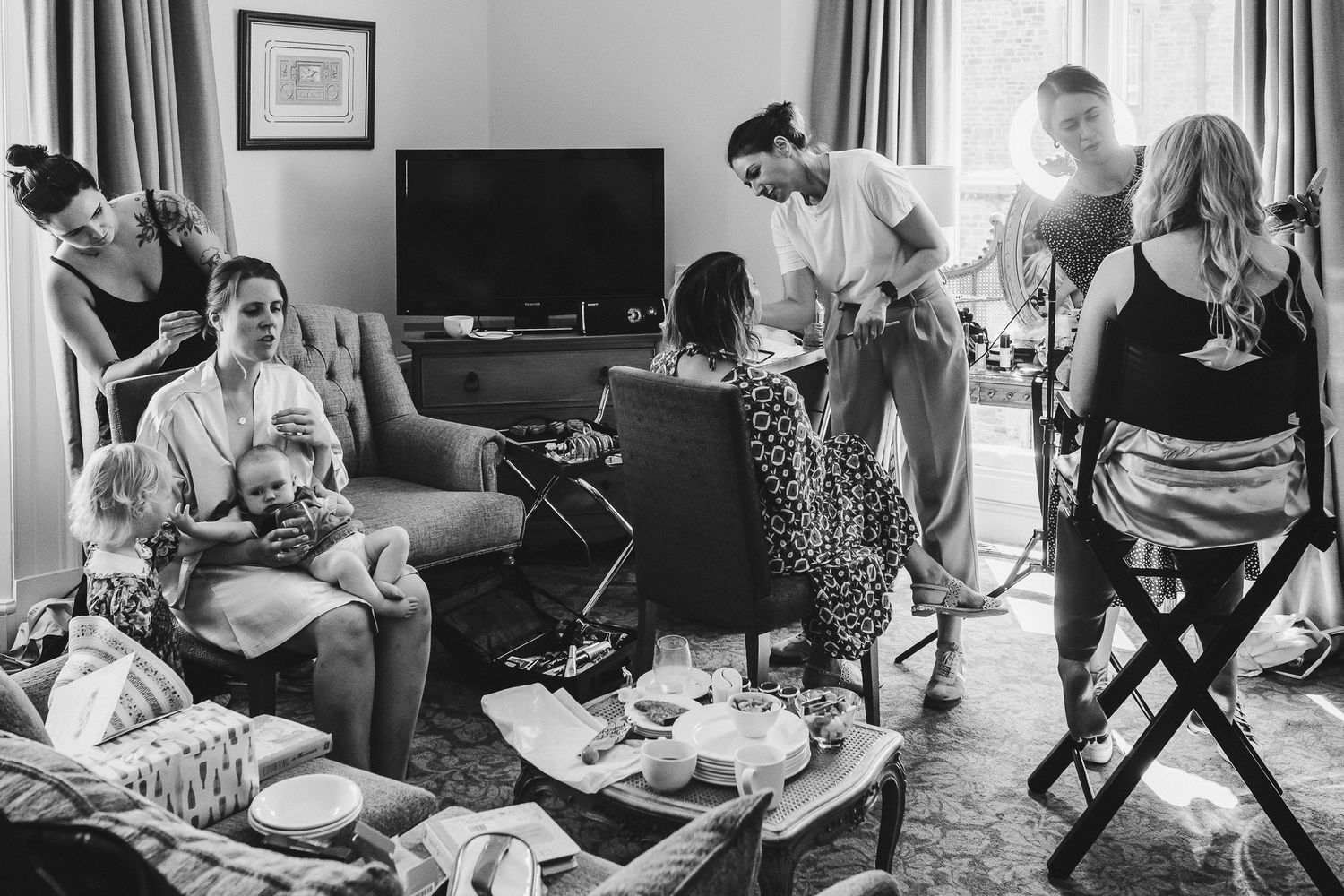 Candid black and white photo of wedding preparations in a living room with family and friends.