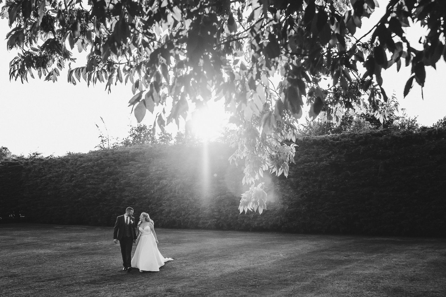 Silhouetted couple walks across sunlit meadow during sunset wedding photography.