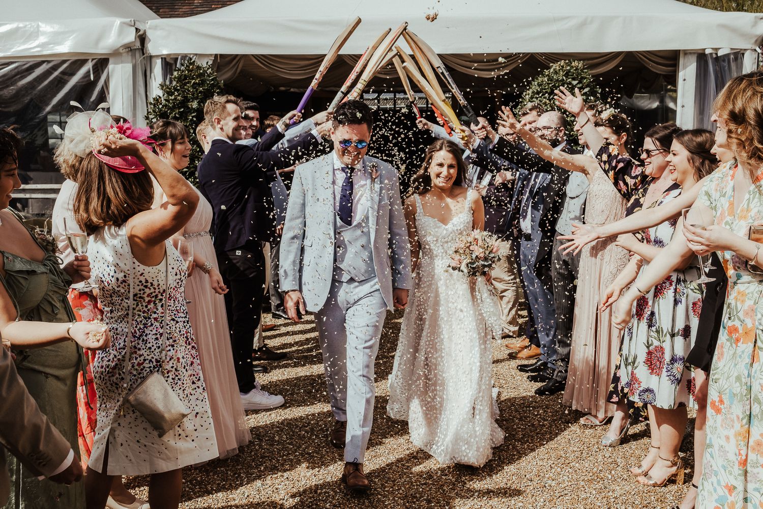 Wedding guests create a tunnel of celebration while a couple walks beneath raised arms in a joyful exit.