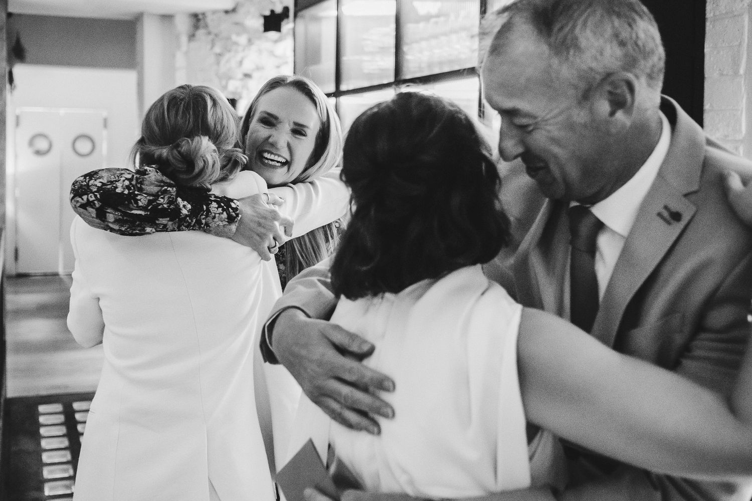 Black and white photo capturing emotional group hug during wedding celebration.