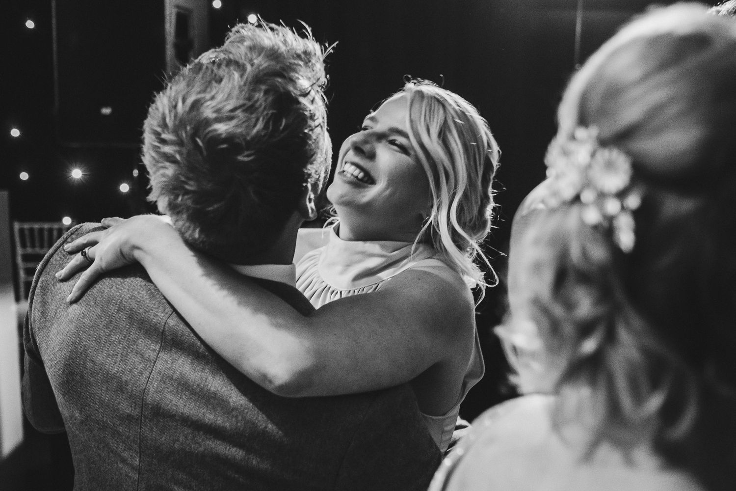 A candid black and white photo capturing an emotional moment of dancing and laughter at a wedding reception.