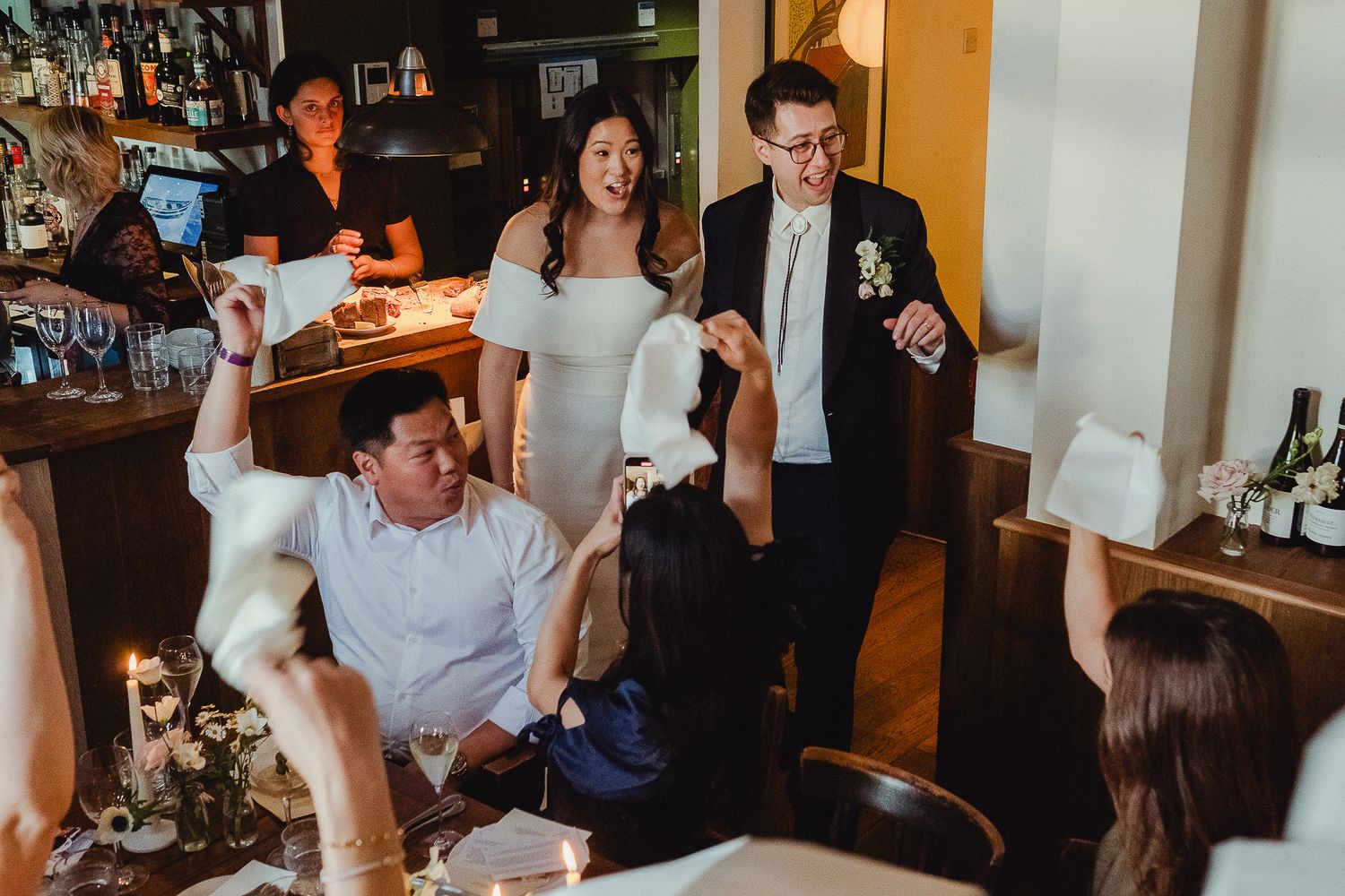 A group of people laughing and socializing at a casual gathering in a dimly lit restaurant or bar setting.