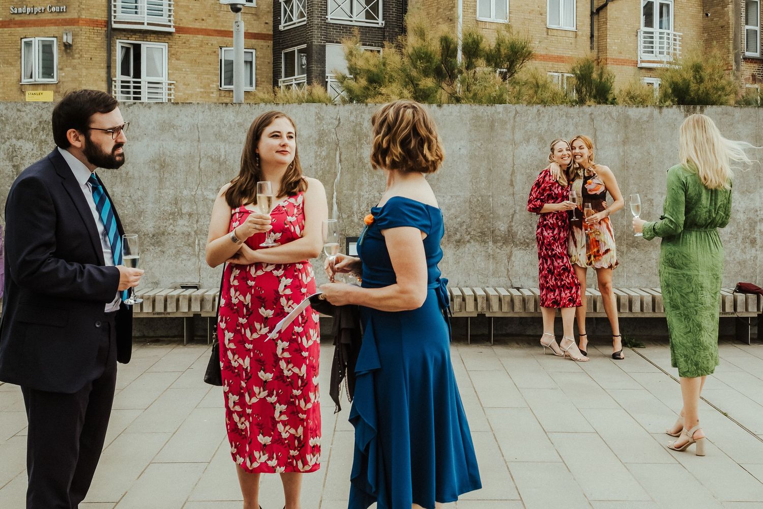 Wedding guests in colorful dresses chatting during an outdoor reception.