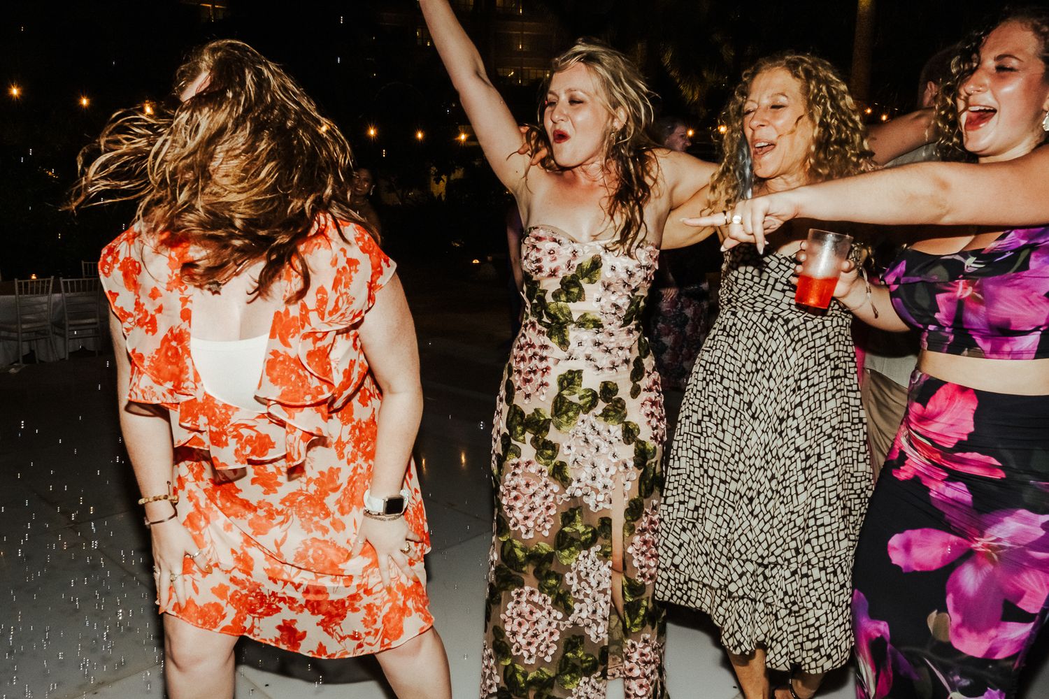 Guests in floral dresses dance with abandon at a lively outdoor party.