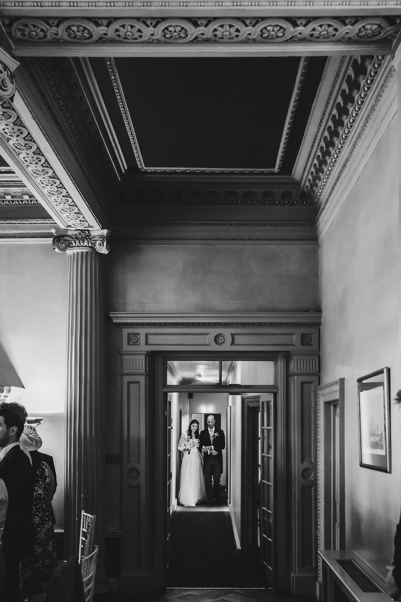 A classic black and white wedding photo through an ornate doorway with detailed architectural moldings.