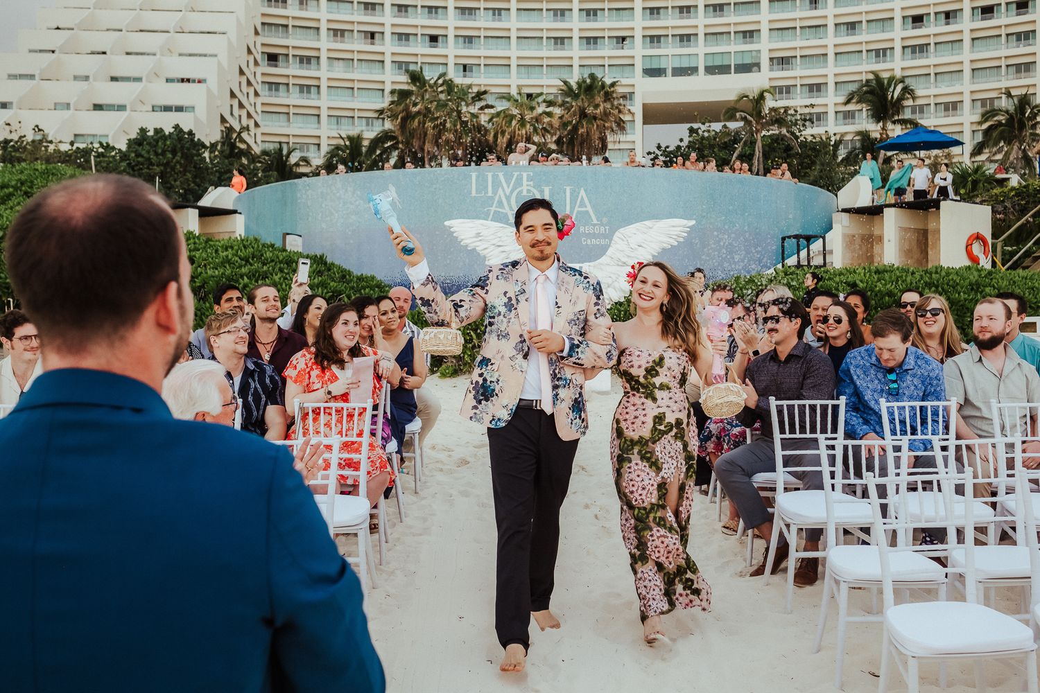 Wedding party members walking down the aisle at an outdoor beachfront ceremony.