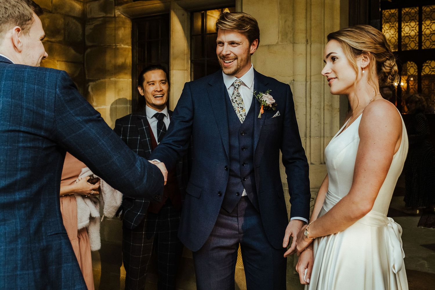 Wedding couple and guests interacting in grand architectural setting with warm lighting.
