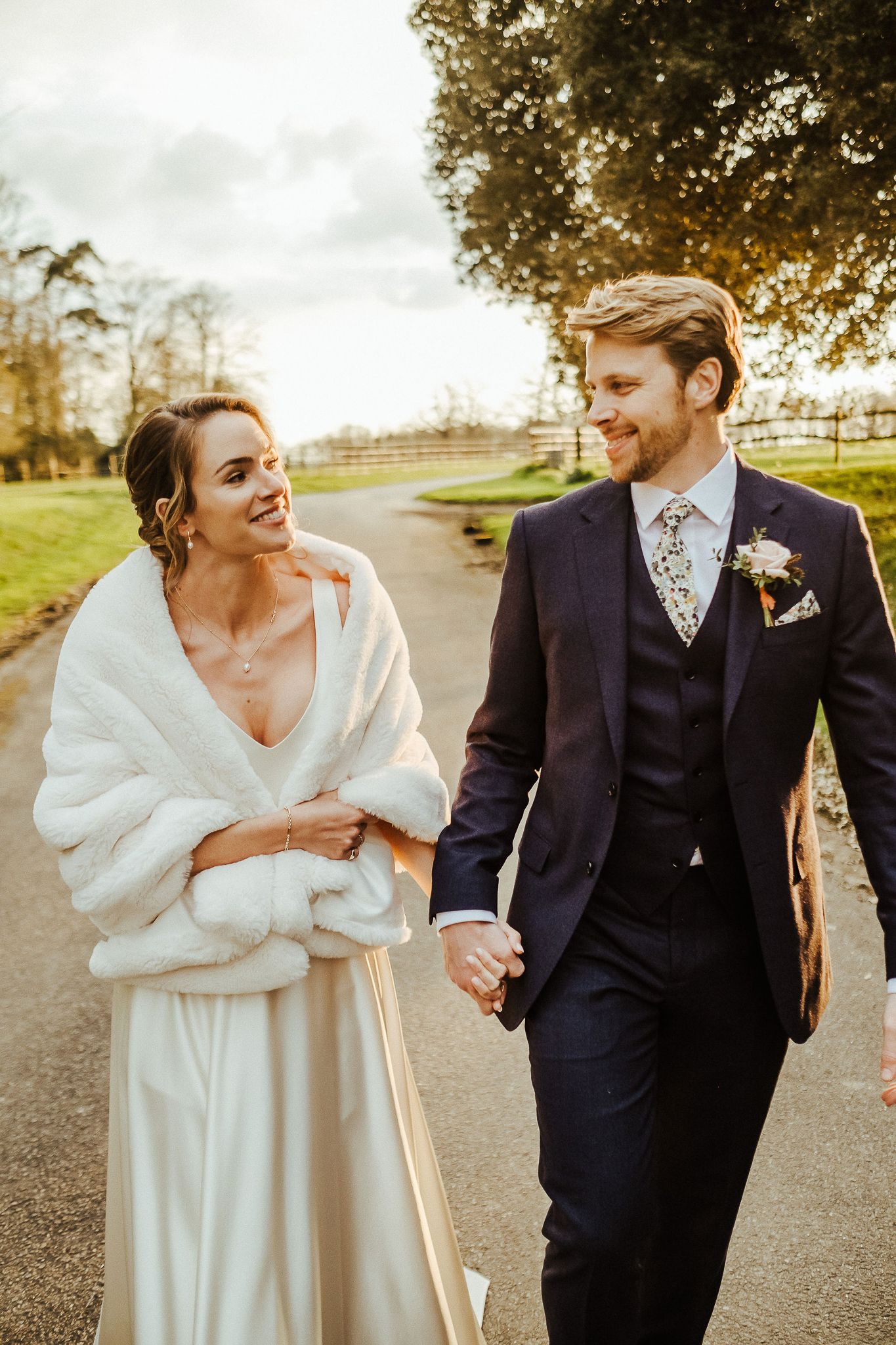 Couple walks together along a path while sharing joyful moments in their wedding attire.