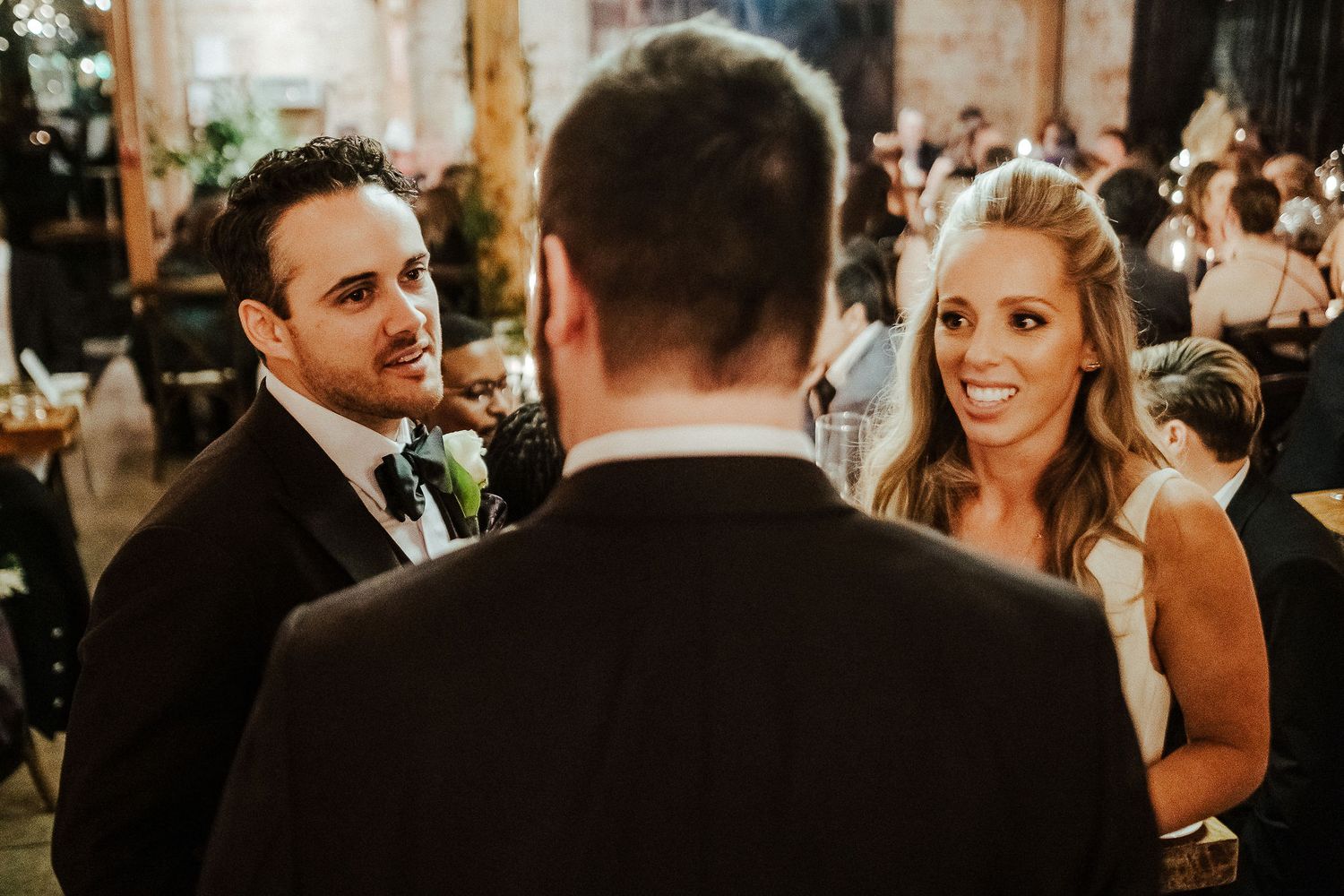 Guests share conversation during golden-hour wedding reception in rustic venue.