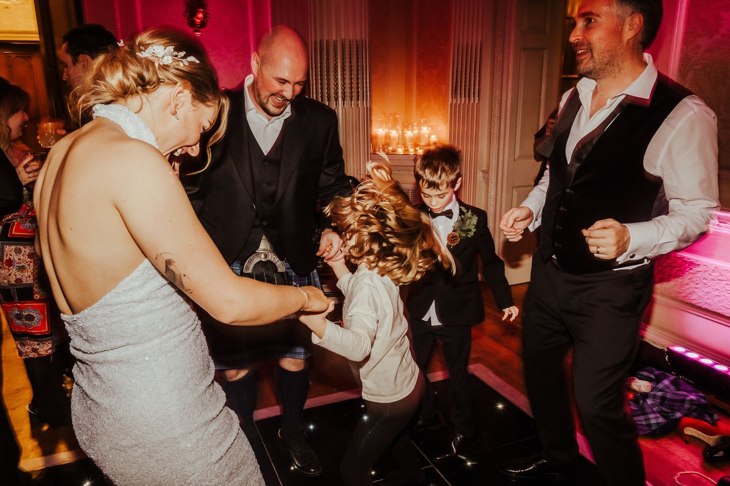 Wedding guests dance and celebrate in an elegantly lit reception hall.