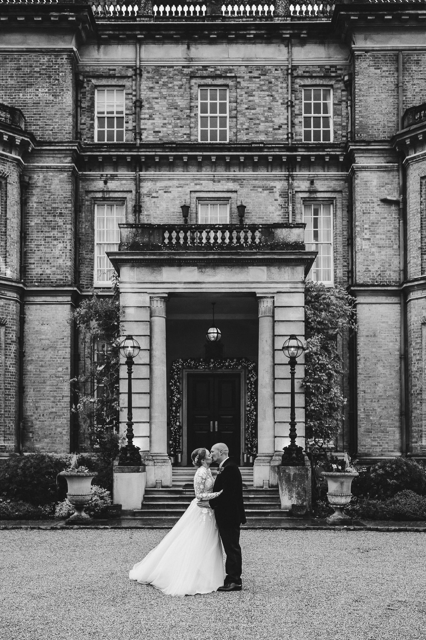 A couple shares a romantic moment outside a grand historic mansion with elegant stone architecture and columns.