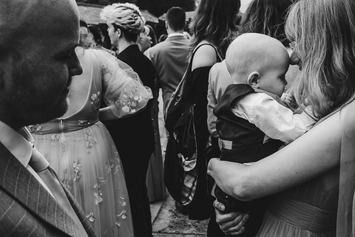 Wedding guests mingling at reception with baby being held in foreground.