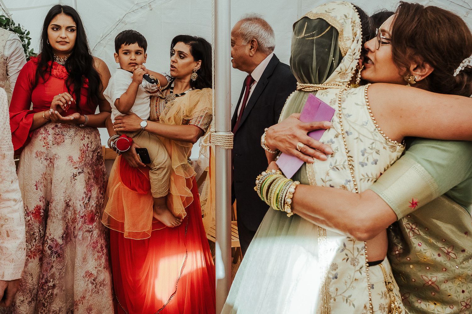 Emotional wedding reception scene with guests in colorful attire sharing embraces.