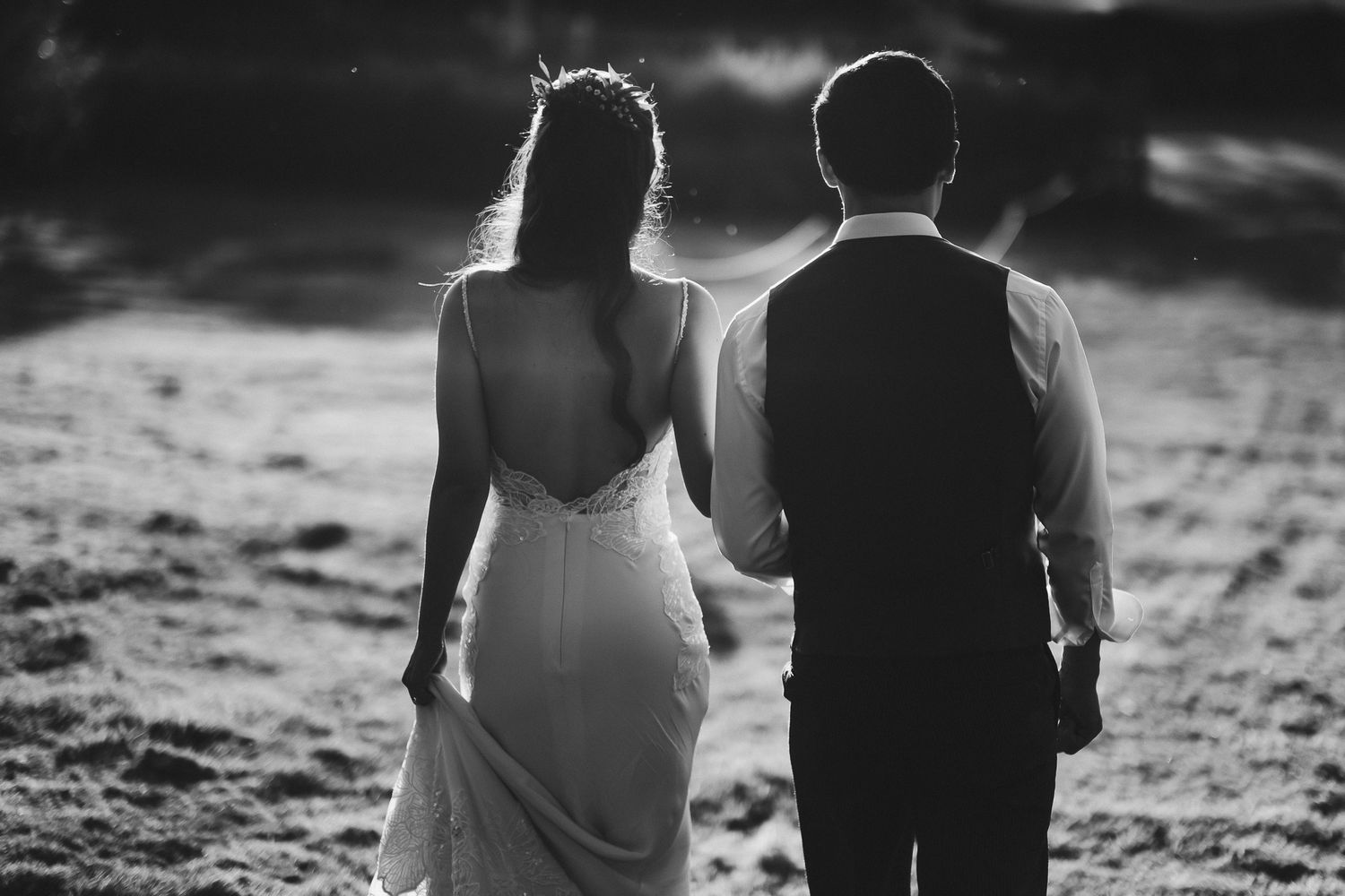 Black and white photo of newlyweds walking together at sunset with dramatic lighting.