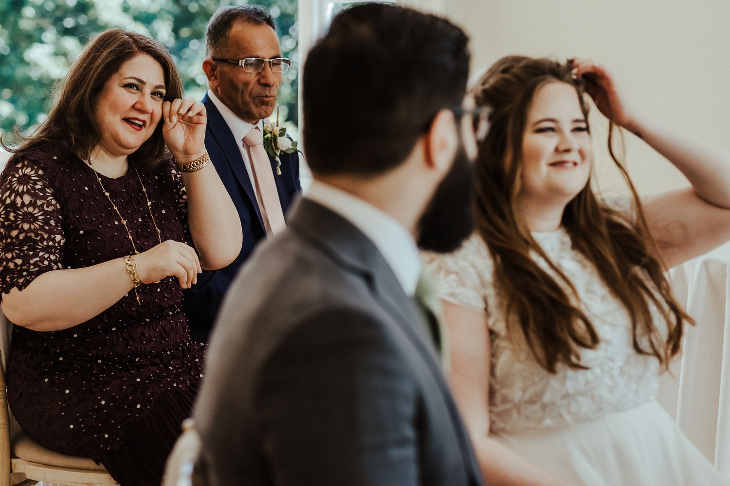 Wedding guests share joyful laughter during an emotional moment at an indoor ceremony.