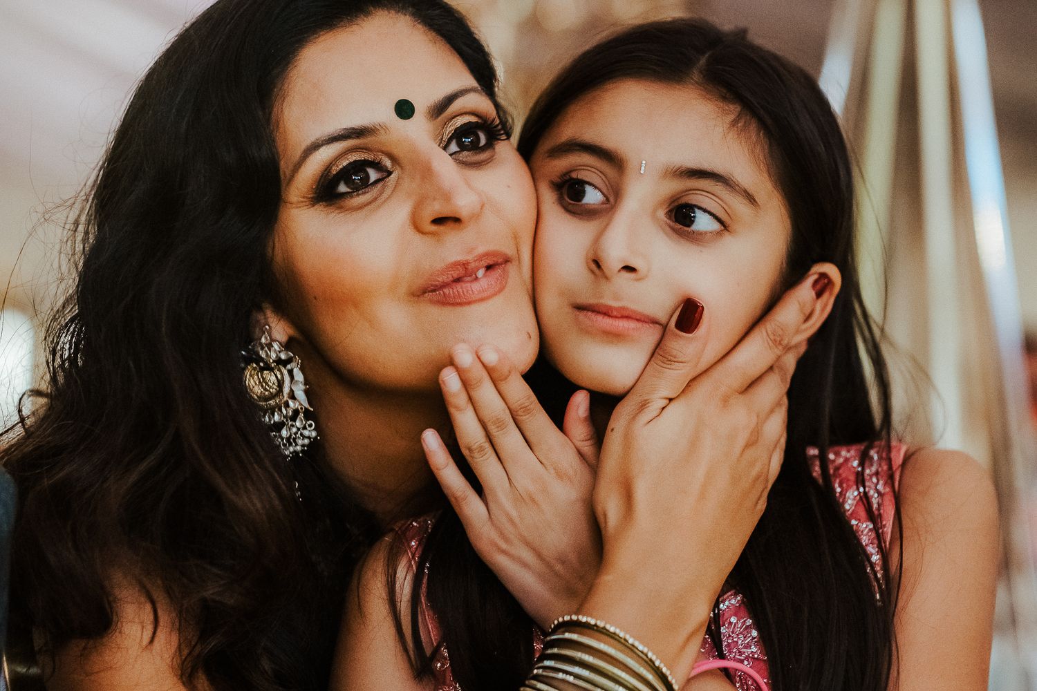 Two women wearing traditional Indian attire and jewelry pose playfully together in a close-up portrait.
