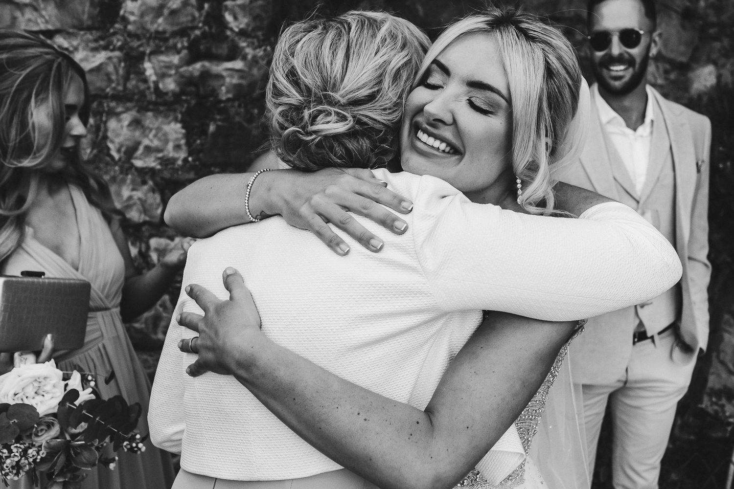 Two wedding guests share a joyful emotional embrace during an outdoor celebration.