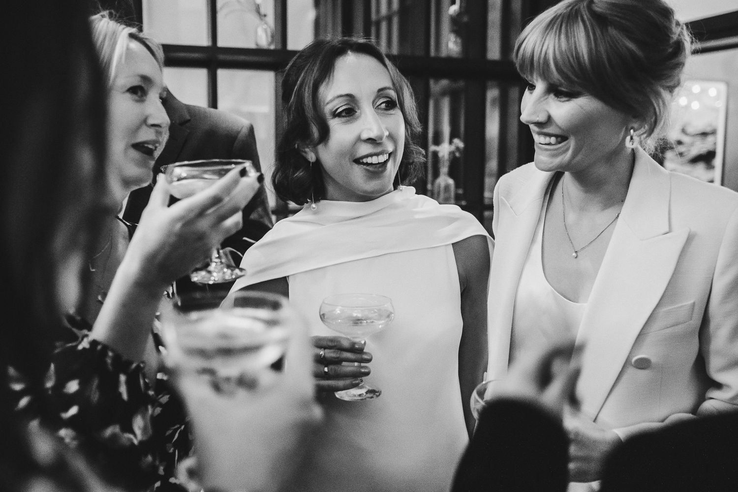 Black and white photo of wedding guests sharing drinks and laughs during the reception celebration.