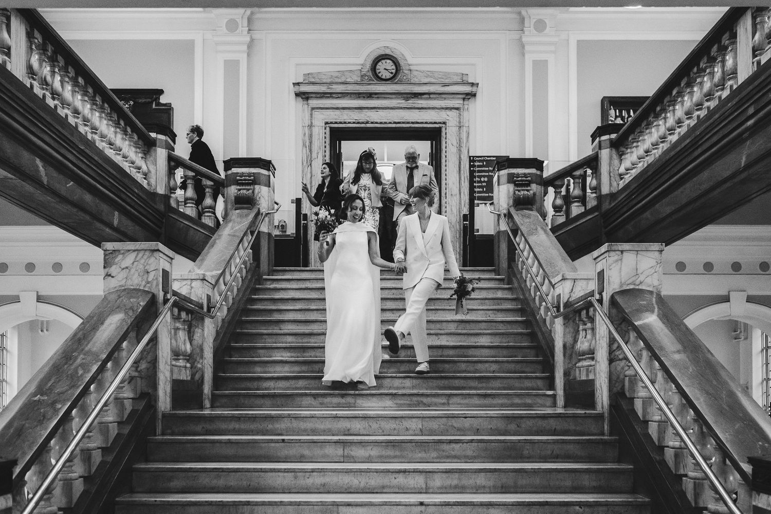 Elegant black and white photo of couple descending grand staircase during wedding ceremony.