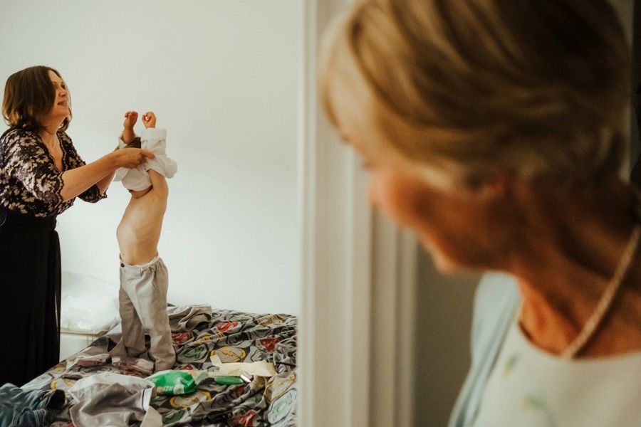 Mother helping young child get dressed in morning light through window.