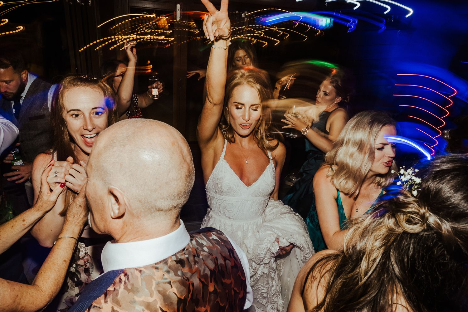 Wedding guests dancing energetically under blue nightclub lighting on a crowded dance floor.