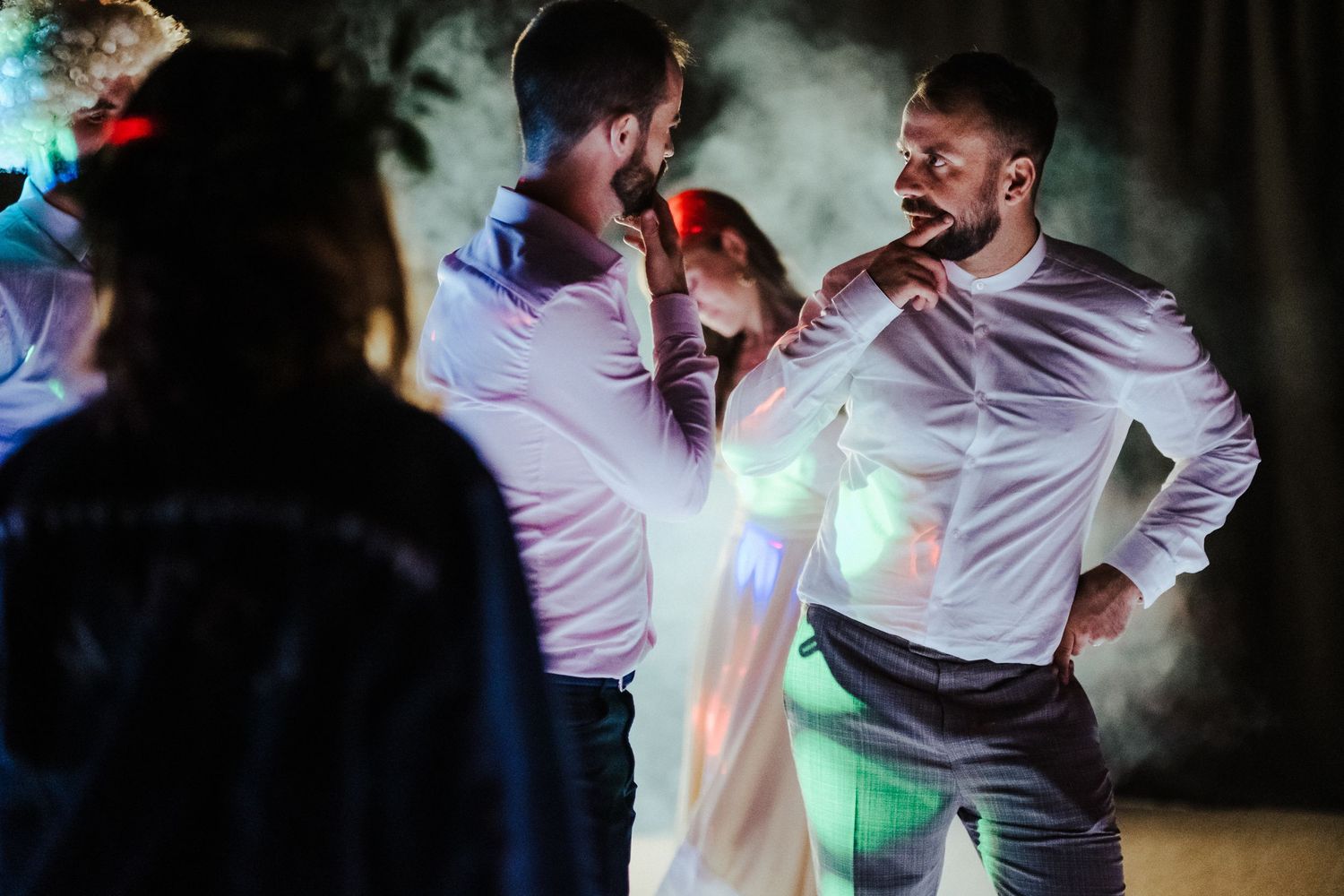 Wedding party dancing energetically on dimly lit dance floor with atmospheric smoke effects.