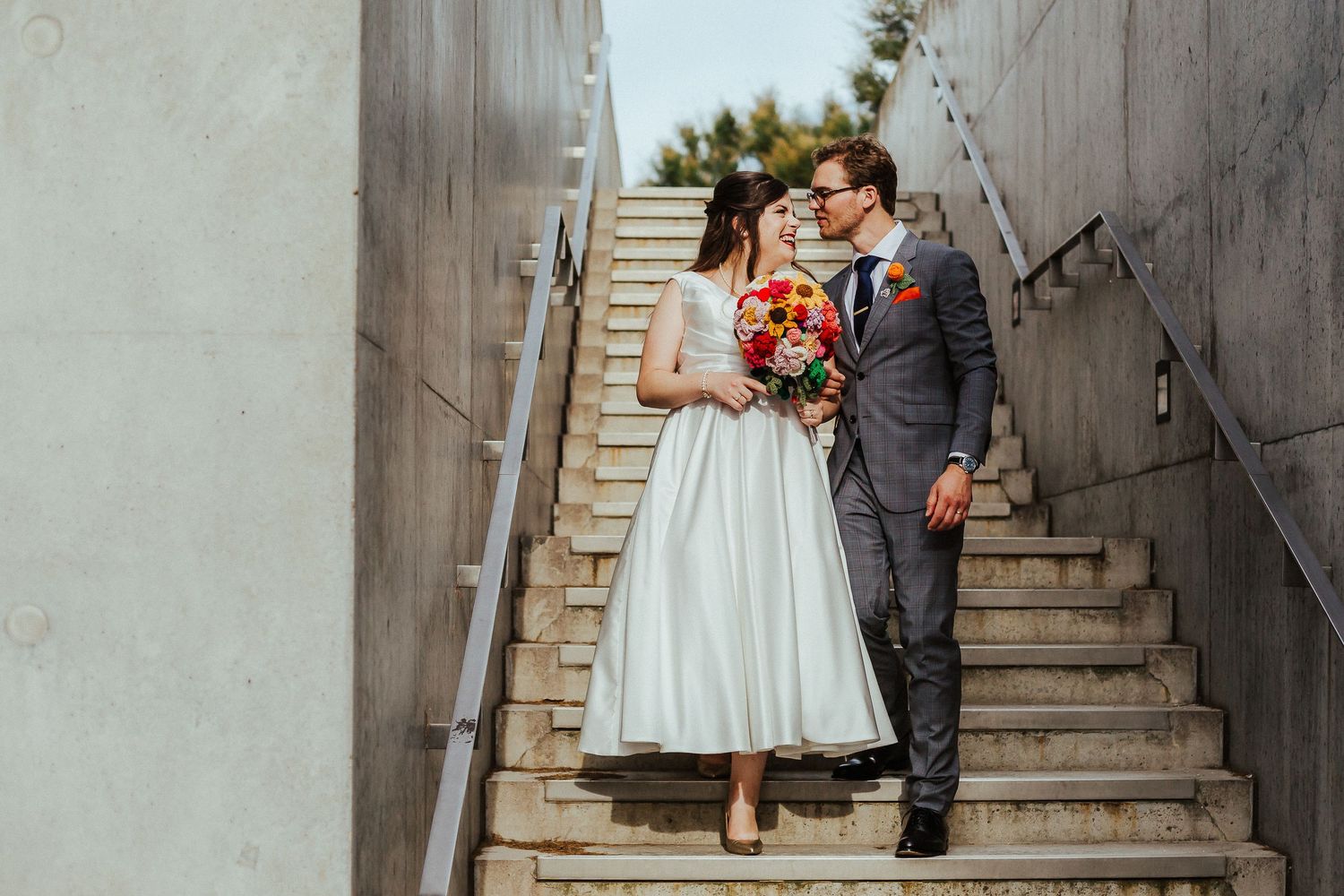 Romantic wedding portrait of couple on concrete staircase with colorful bouquet.