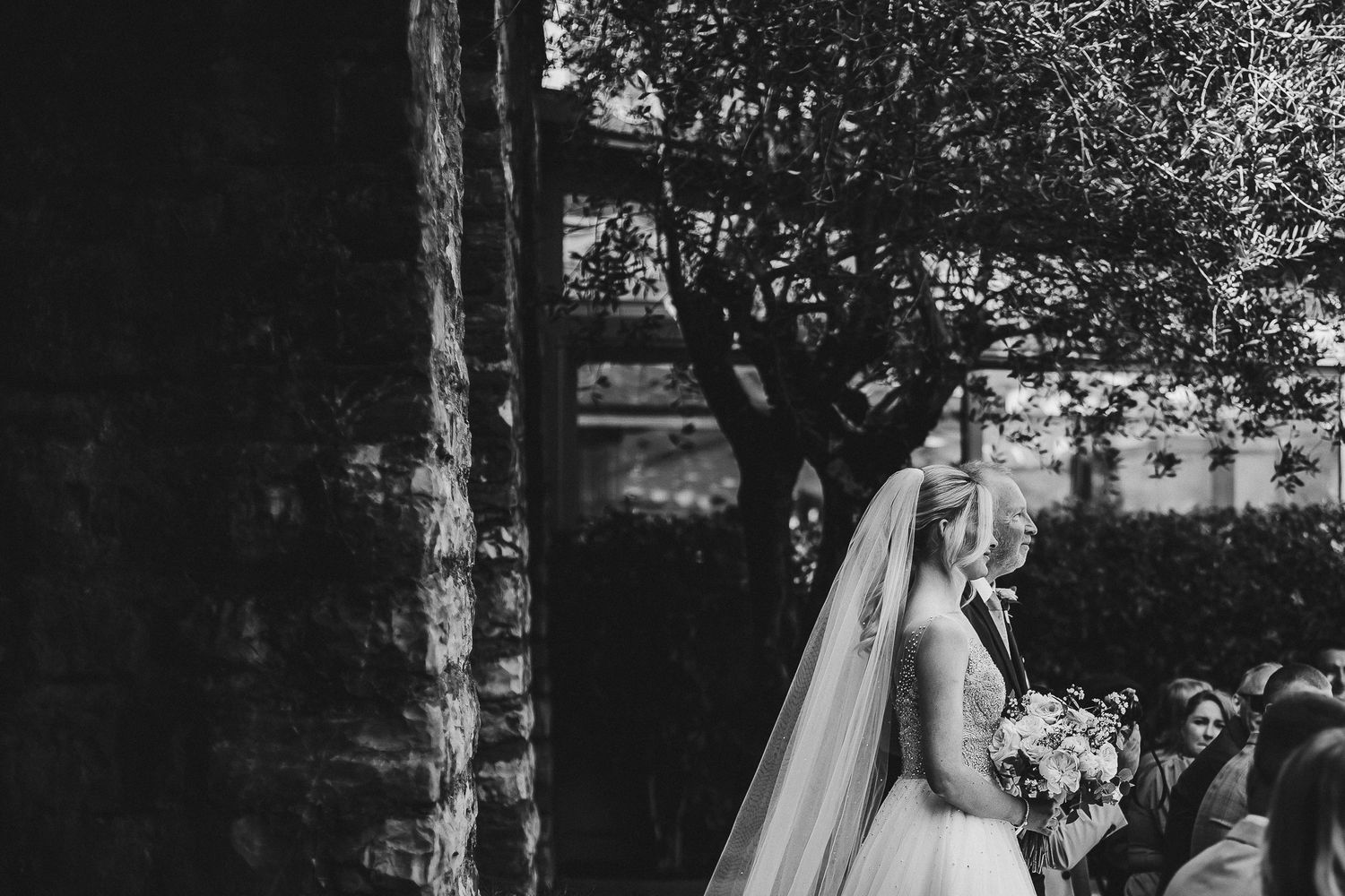 Black and white photo of bride in elegant dress during outdoor wedding ceremony.