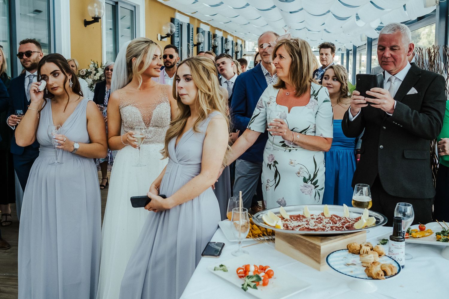 Wedding party guests mingling around a buffet table with appetizers and drinks.