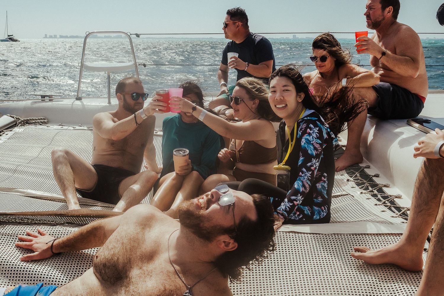 Group of friends enjoying drinks while lounging on a boat deck in the sunshine.