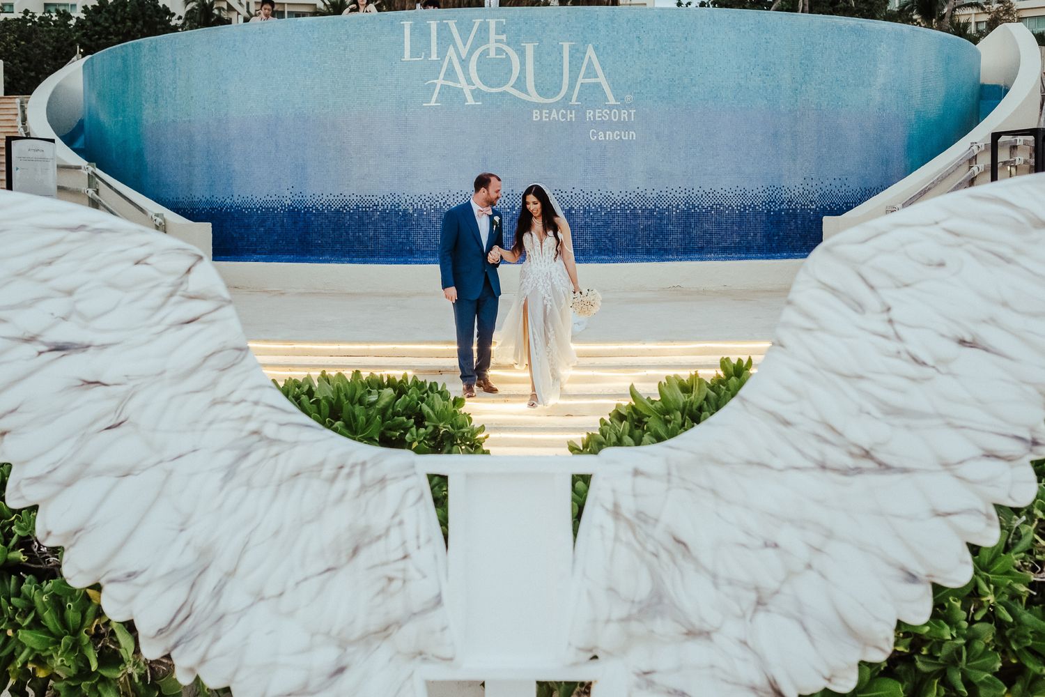 Newlyweds pose in front of decorative white wings at Live Aqua resort.