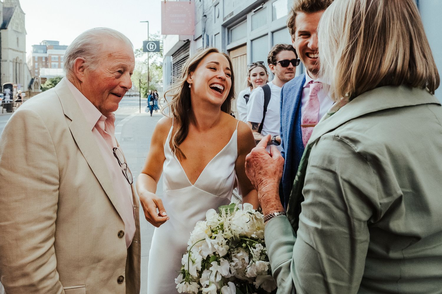 Joyful celebration outside with white bouquet and formal attire on a city street.