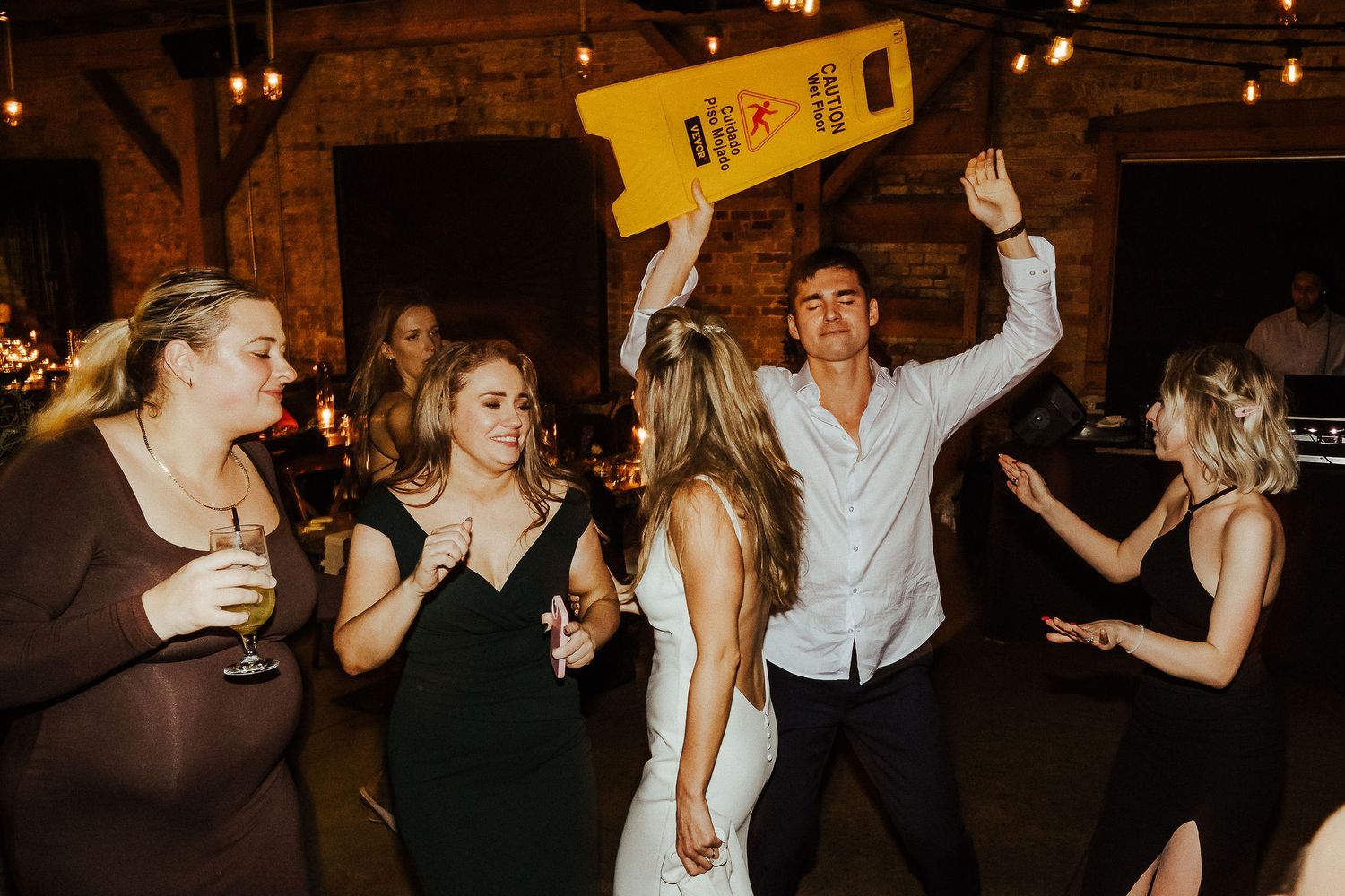 Partygoers dancing and having fun in a dimly lit reception venue during a celebration.