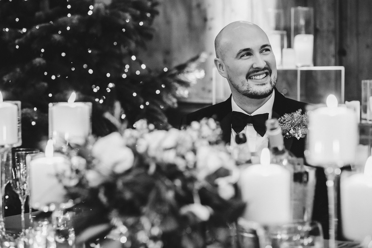 Black and white photo of a wedding reception with glowing candles and floral centerpieces on an elegant table.