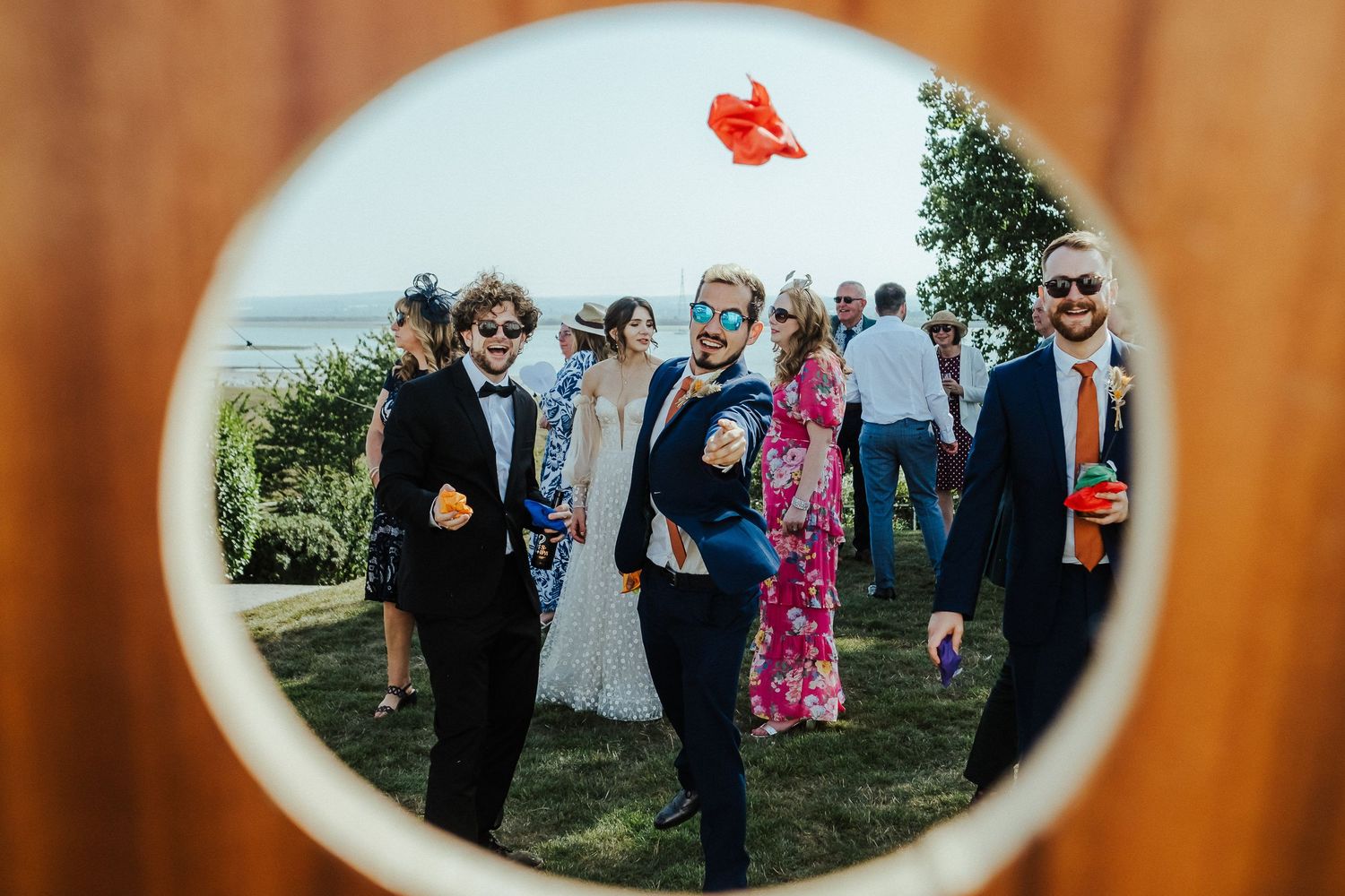 Fish-eye lens capture of wedding guests celebrating outdoors with red balloon floating above.