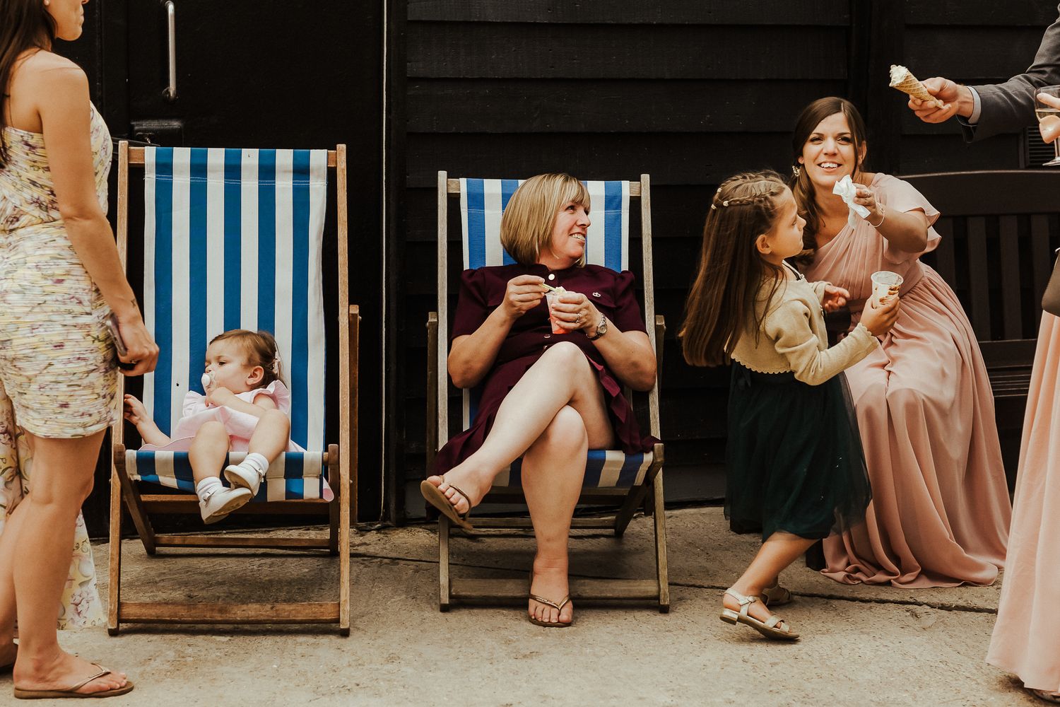 Wedding guests relaxing on casual striped outdoor furniture during a reception.