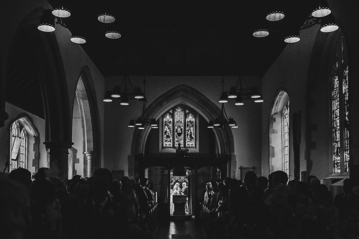 Black and white photo of a wedding ceremony in a grand church with dramatic lighting.