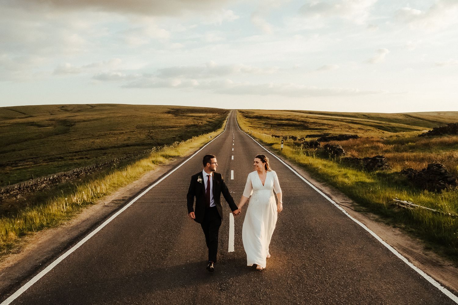 Couple walking down an empty rural road at sunset with dramatic lighting.