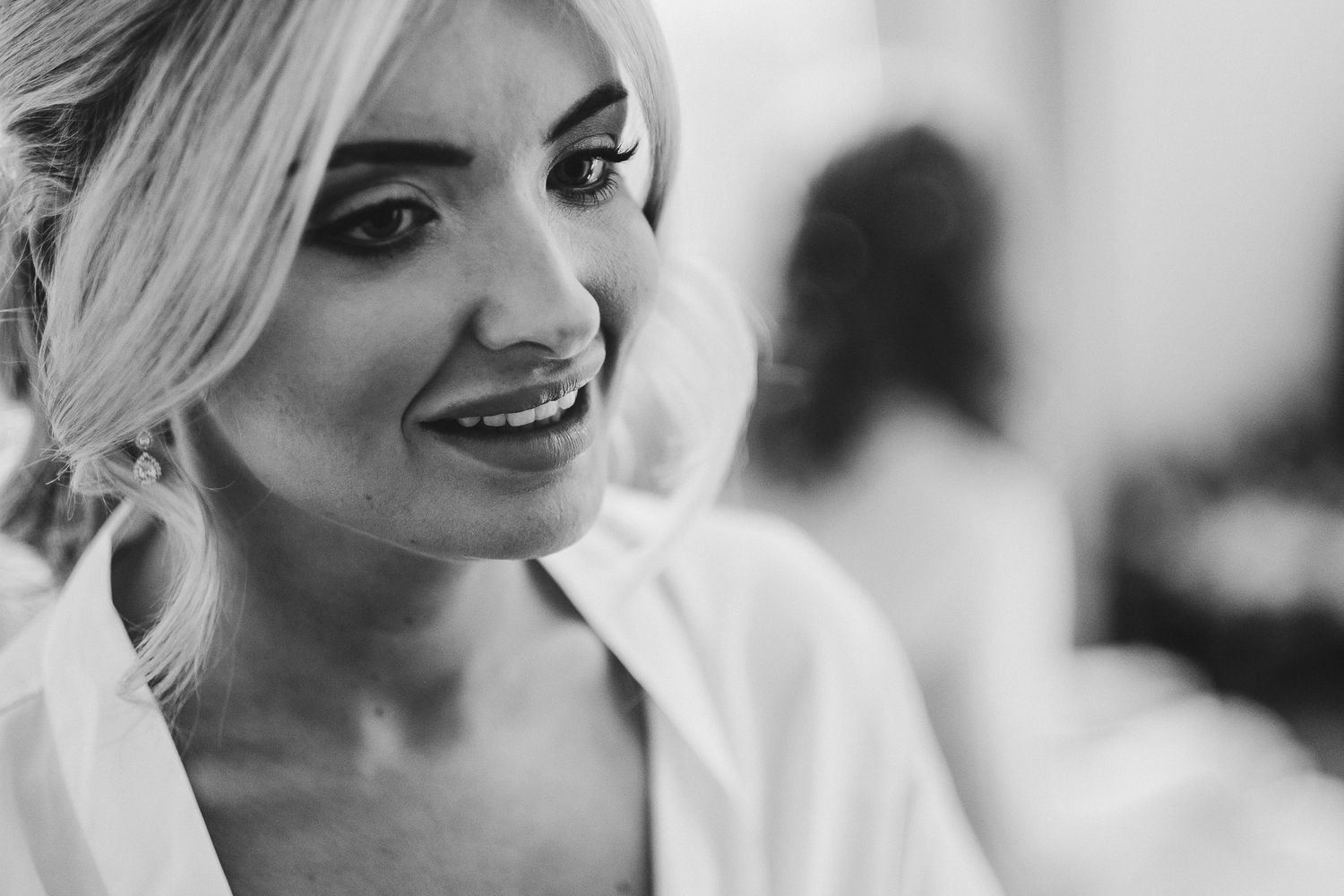 Close up black and white portrait of smiling woman in white robe during wedding preparations.