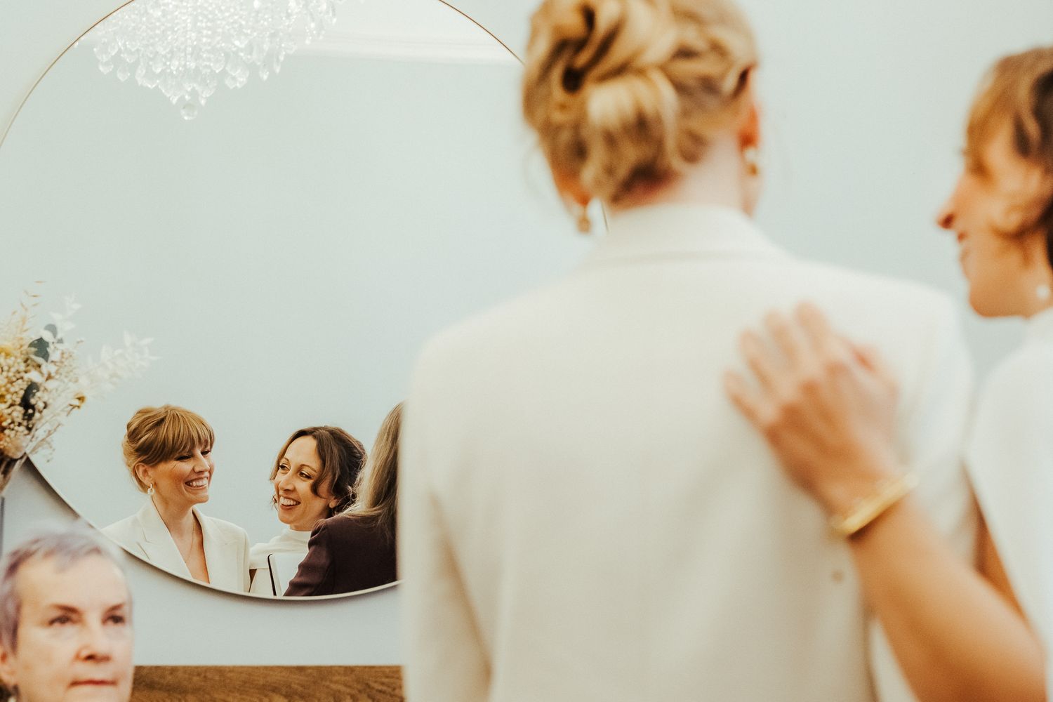 A reflection in a round mirror captures a tender wedding moment against a light background.