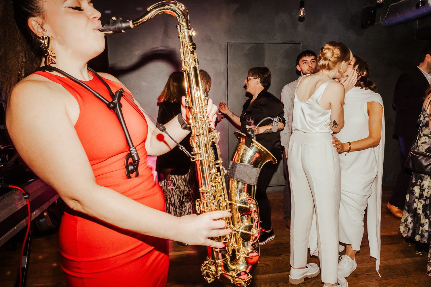 Musician playing saxophone during wedding reception with dramatic lighting.