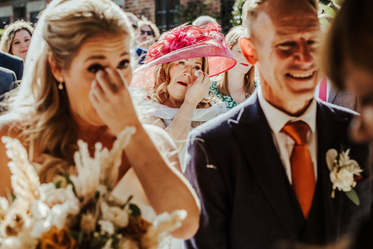 Emotional candid moment at outdoor wedding with guests in formal attire.